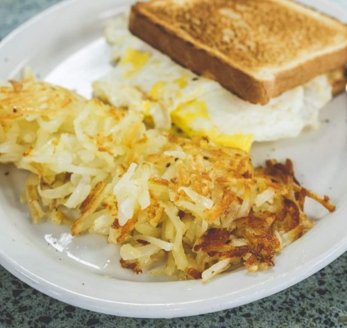 A plate with crispy hash browns, a fried egg, and toasted bread.