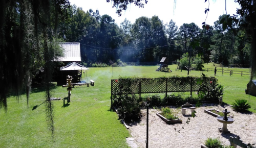 A serene outdoor scene featuring a grassy area, a small building, and a garden with plants and a stone path.