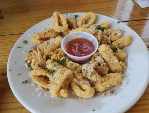 A plate of crispy fried calamari garnished with parsley and served with a small cup of marinara sauce.