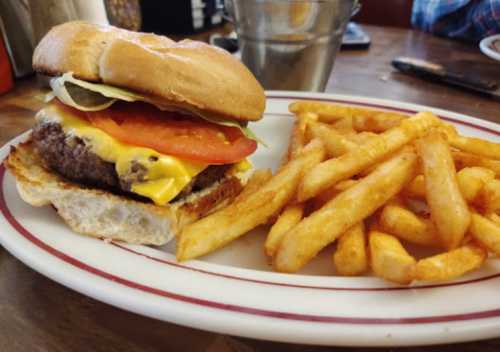 A cheeseburger with lettuce, tomato, and pickles on a bun, served with a side of golden French fries.