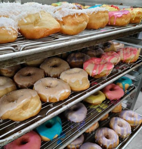 A display of assorted donuts on racks, featuring glazed, frosted, and coconut-topped varieties in vibrant colors.
