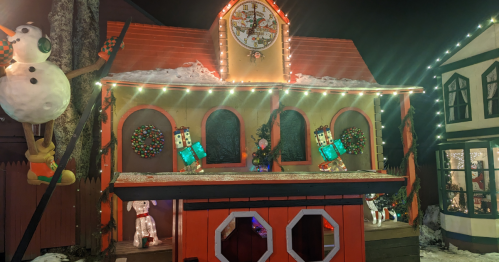 A festive building decorated with lights, wreaths, and holiday figures, set in a snowy winter scene.