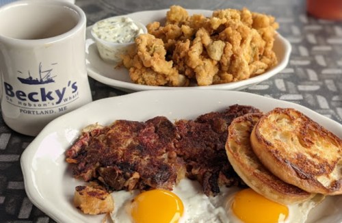A plate of breakfast with two eggs, hash browns, and toast, alongside a bowl of fried clams and a coffee mug.