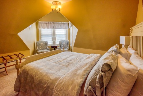Cozy bedroom with a large bed, two armchairs by a window, and warm yellow walls.