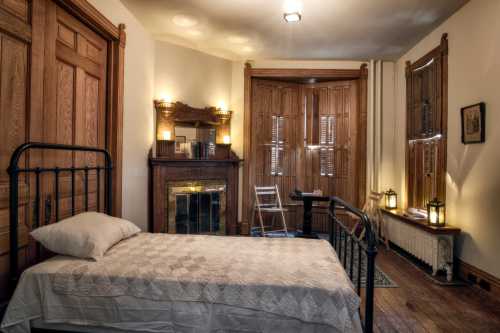 A cozy room featuring a bed, wooden doors, a fireplace, and a small desk with lanterns for lighting.