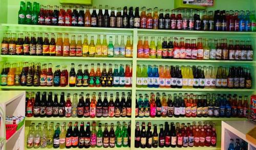 A colorful display of various soda bottles arranged on shelves against a green background.