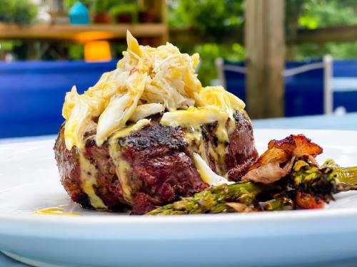 A grilled steak topped with crab meat and sauce, served with asparagus on a white plate.
