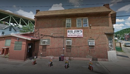 Exterior of Big Jim's, a brick building with a large sign, featuring air conditioning units and flower pots at the entrance.