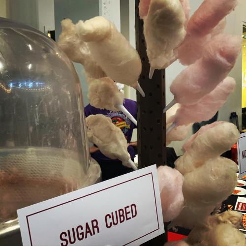A display of cotton candy on sticks, with a sign reading "Sugar Cubed" in a festive setting.
