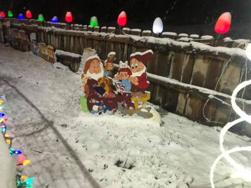 Snow-covered yard with colorful lights and a festive display featuring cartoon characters sitting together.