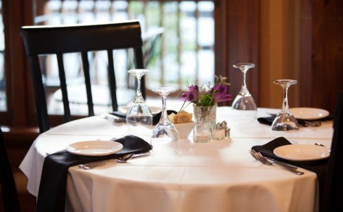 A elegantly set dining table with white tablecloth, plates, glasses, and a small vase of flowers.