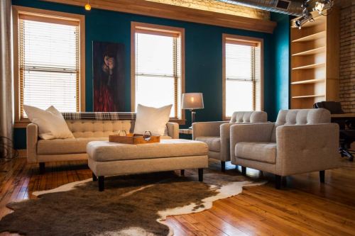Cozy living room with a blue wall, light furniture, a coffee table, and large windows letting in natural light.