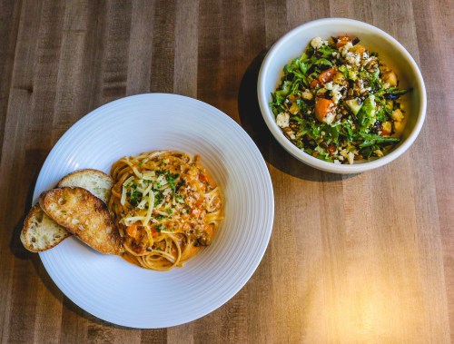 A plate of spaghetti with sauce and two slices of toasted bread, alongside a bowl of mixed salad with grains and vegetables.