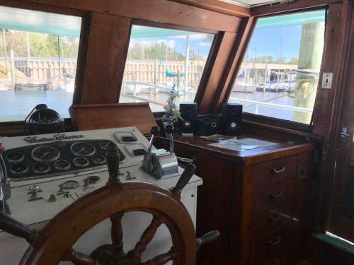 Interior of a boat's cabin featuring a steering wheel, control panel, and windows overlooking a marina.