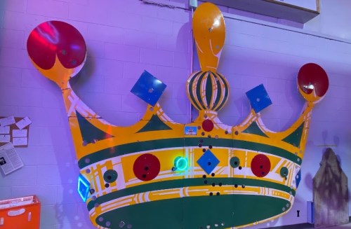 A large, colorful crown sculpture with red, blue, and yellow accents, illuminated with purple lighting.