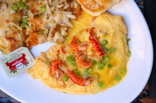 A plate featuring a shrimp omelet topped with green onions, alongside hash browns and a biscuit.