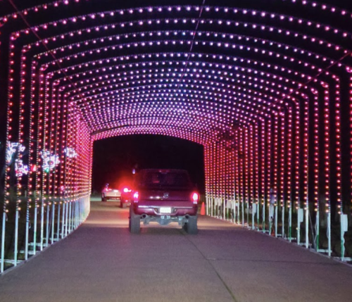 A truck drives through a brightly lit archway of red and purple lights at night.