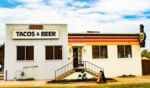 A restaurant building with a sign reading "Tacos & Beer," featuring a staircase and outdoor seating area.