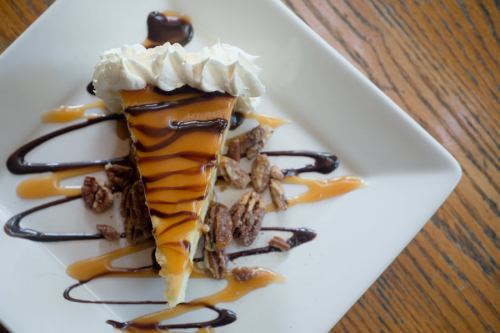 A slice of pie topped with whipped cream, drizzled with chocolate and caramel, on a plate with crushed nuts.