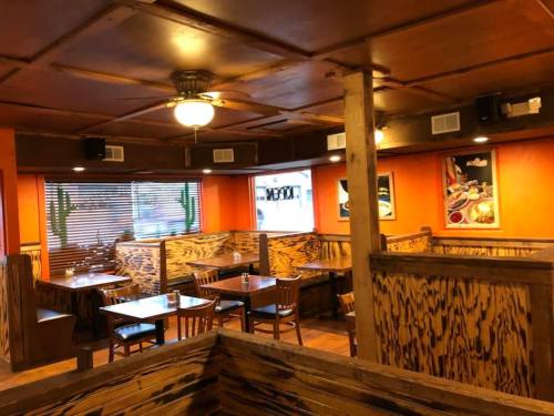Cozy restaurant interior with wooden booths, tables, and orange walls, featuring a ceiling fan and window blinds.