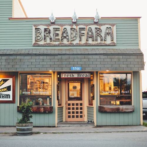 A quaint bakery storefront with a sign reading "Breadfarm," featuring large windows and a welcoming entrance.