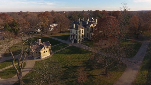 Aerial view of a large historic mansion surrounded by trees and pathways in a park during autumn.