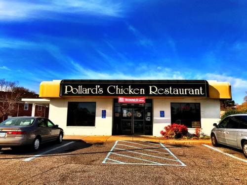 Exterior of Pollard's Chicken Restaurant with a bright sign, parked cars, and a clear blue sky.