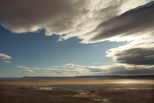 A serene landscape featuring a vast sky with clouds and a calm body of water reflecting soft light.