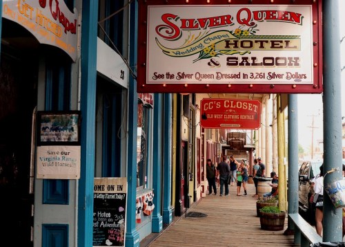 Historic storefronts line a wooden walkway, featuring signs for the Silver Queen Hotel & Saloon and CC's Closet.