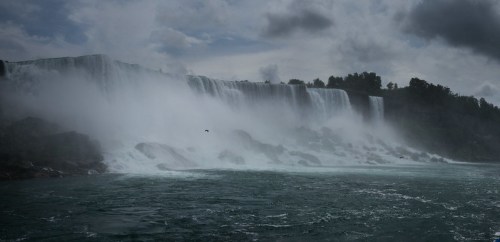 A misty view of a waterfall cascading over rocky cliffs under a cloudy sky.