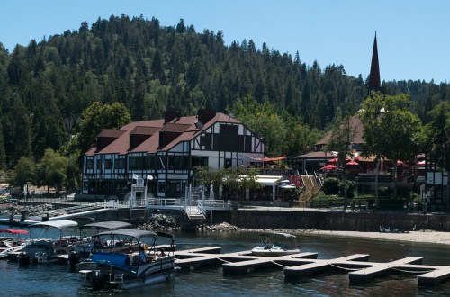 A lakeside view of a charming building with a steep roof, surrounded by trees and boats docked along the shore.