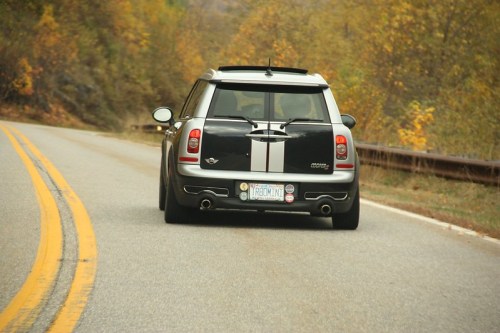 A black and silver car drives down a winding road surrounded by autumn foliage.