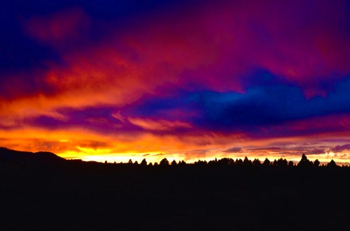 Vibrant sunset with purple and orange hues over a dark silhouette of trees and hills.