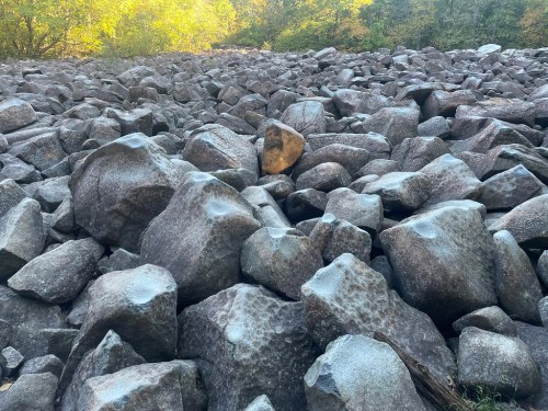 A rocky landscape filled with large, uneven boulders under soft sunlight and surrounded by greenery.