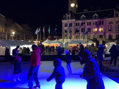 A nighttime ice skating rink with children and adults skating, surrounded by festive tents and lights.