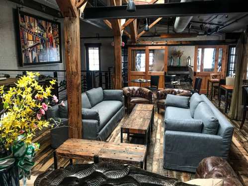 Cozy interior with gray sofas, wooden tables, and rustic decor, featuring exposed beams and warm lighting.