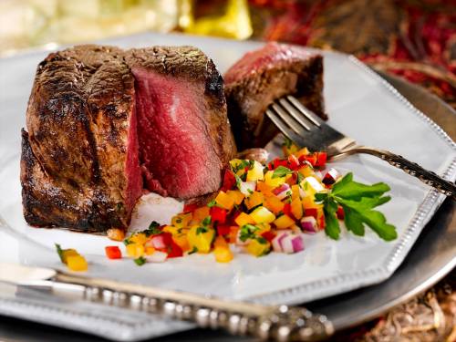A perfectly cooked beef roast with a side of colorful diced vegetables on a decorative plate.