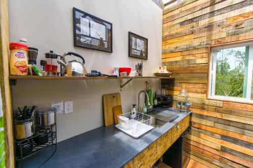 A cozy kitchen with wooden walls, a black countertop, and various kitchen appliances and utensils neatly arranged.