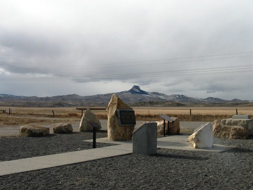 A rocky monument with informational plaques, set against a cloudy sky and distant mountains in a rural landscape.