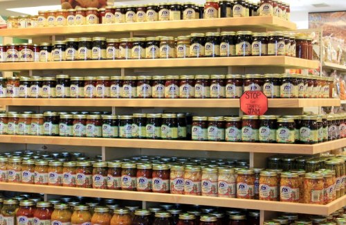 A display of neatly arranged jars of various jams and preserves on wooden shelves in a store.
