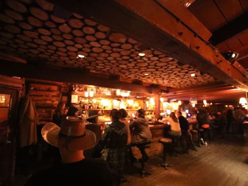 A cozy bar interior with wooden decor, patrons sitting at the bar, and warm lighting creating a welcoming atmosphere.