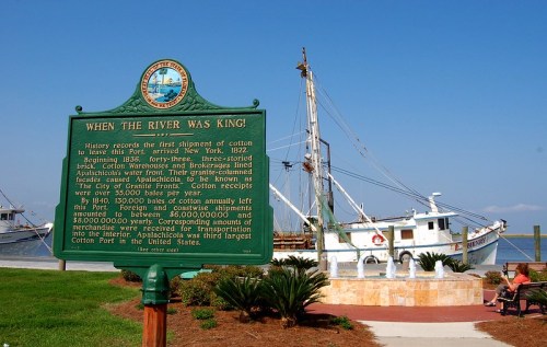 Historical marker about cotton shipping in the 1800s, with a ship and waterfront in the background.