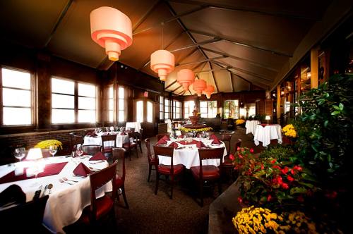 Elegant restaurant interior with round tables, white tablecloths, and warm lighting from hanging lamps. Flowers add color.