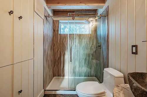 Modern bathroom featuring a glass shower, toilet, and wooden accents with natural light from a window.