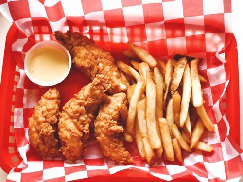 A red checkered basket filled with crispy fried chicken tenders, a small cup of dipping sauce, and golden French fries.
