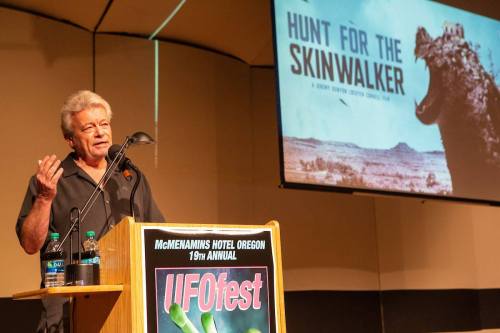 A speaker at a podium discusses "Hunt for the Skinwalker" at the 19th Annual UFOfest in McMenamins Hotel, Oregon.