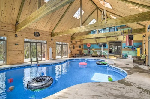 Indoor pool area with wooden beams, colorful decor, and floating toys, surrounded by large windows and natural light.