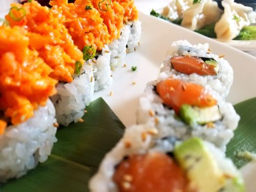 A close-up of sushi rolls, featuring salmon and avocado, with vibrant orange toppings and a side of dumplings.