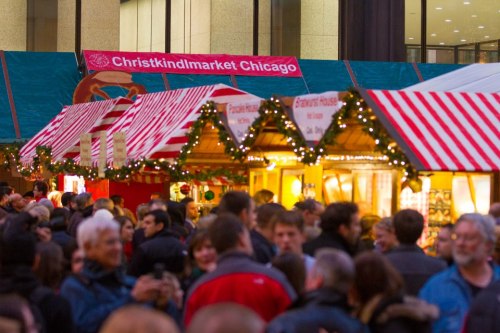 Crowd at Christkindlmarket Chicago, featuring festive stalls with red and white stripes and holiday decorations.