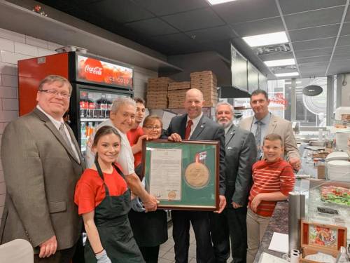 A group of people in a restaurant pose with a framed certificate, celebrating a special occasion.